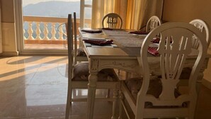 A dining area with a table set for four, chairs, and a view of the outdoors through a window. - The Taal Cottage (Bhimtal)