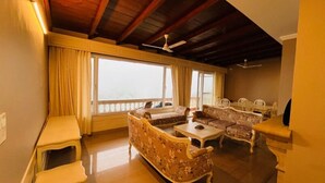 A spacious living room with a high ceiling, large windows, and a balcony. - The Taal Cottage (Bhimtal)