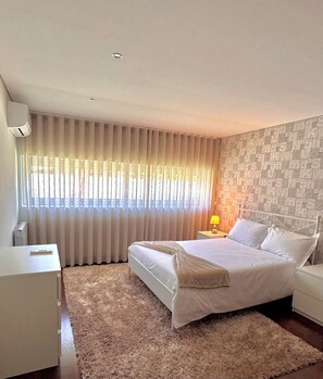 Un dormitorio con cama, mesita de noche, lámpara, radiador y ventana con cortinas.