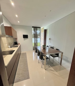 Une cuisine moderne dotée d’un four encastré, un coin repas avec une table et des chaises, et une grande fenêtre offrant une vue sur l’extérieur.