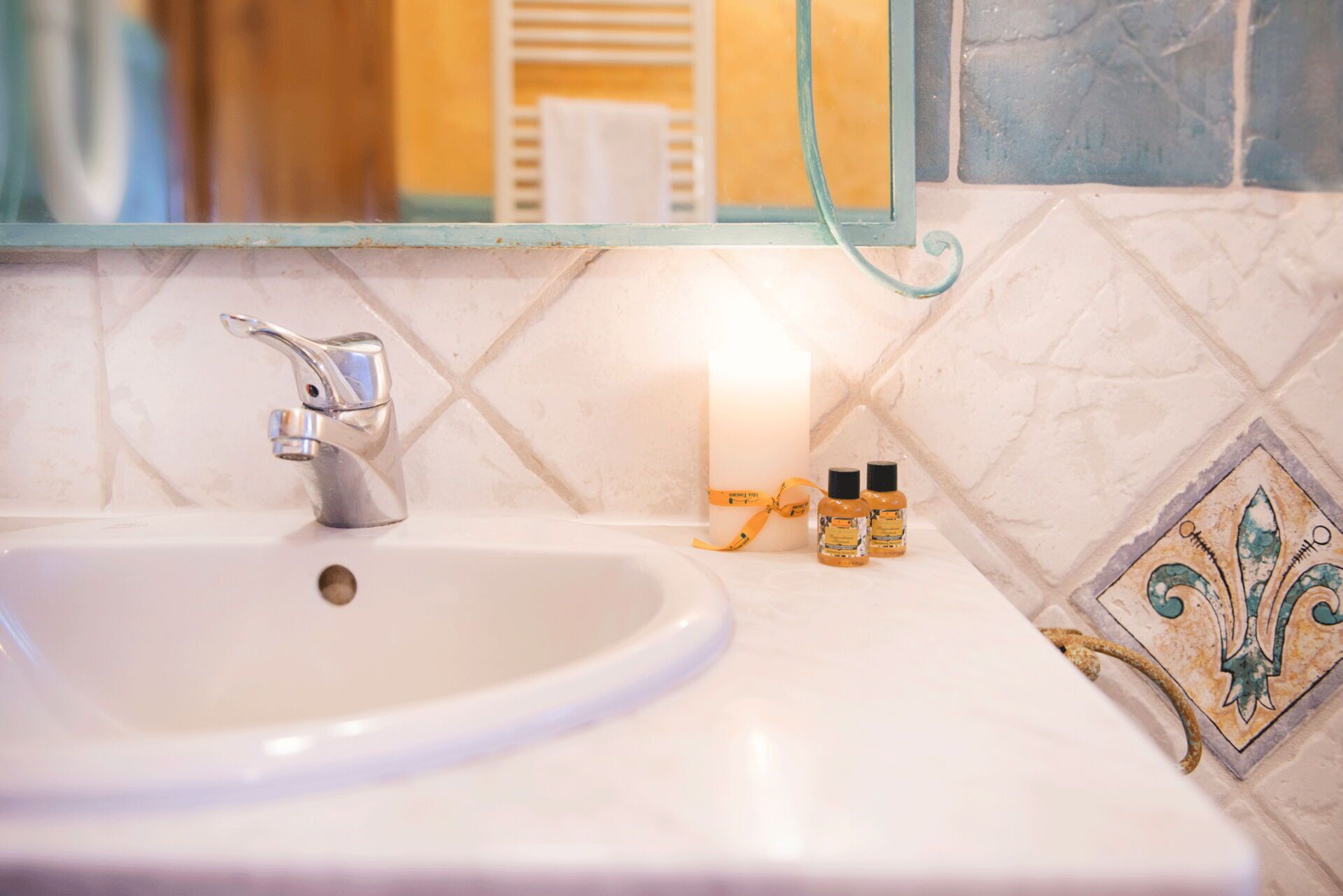 A bathroom sink with a modern faucet, a lit candle, and two small bottles of lotion on the counter.