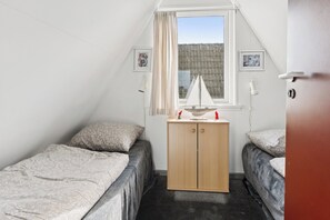 A small, single-room accommodation with two beds, a wooden wardrobe, a window with curtains, and a small sailboat decoration. - Holiday Home Near Beach Fun in Gedser (Gedser)