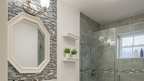 Un bany modern amb un moble de bany blanc, una cabina de dutxa de vidre i un mirall gran amb llums penjades a la paret.
