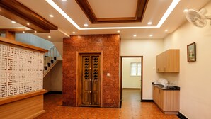 Un couloir avec un escalier en bois, un mur décoratif et un coin cuisine équipé de placards et d’un ventilateur.