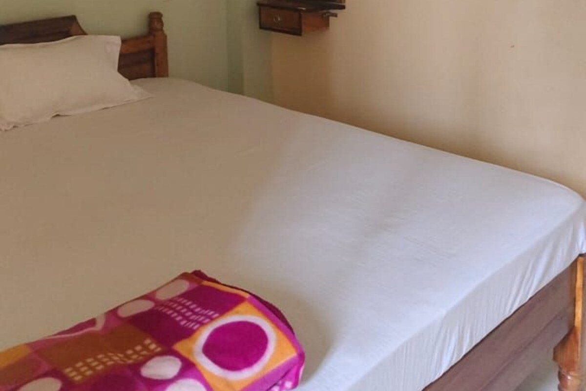 A hotel room with a single bed, a wooden headboard, a bedside table, and a mirror on the wall.