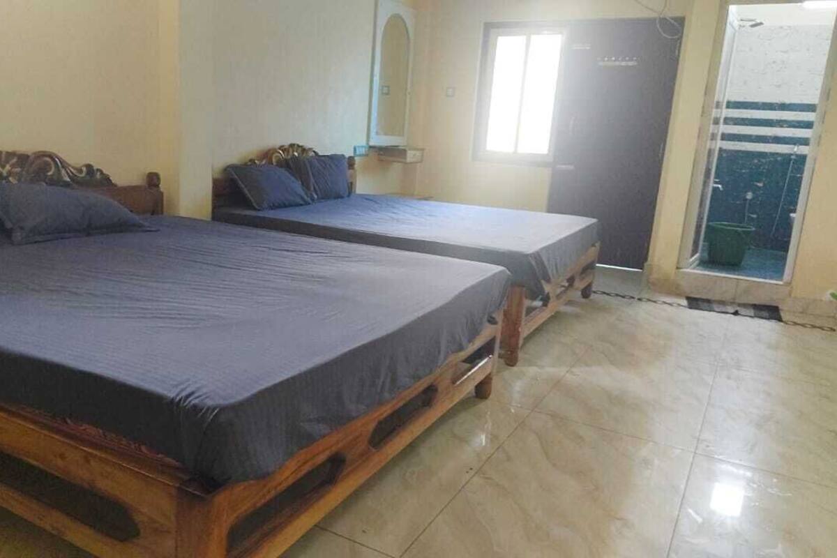 A room with two wooden beds with dark mattresses and headboards, a small window, and a door leading to a balcony.