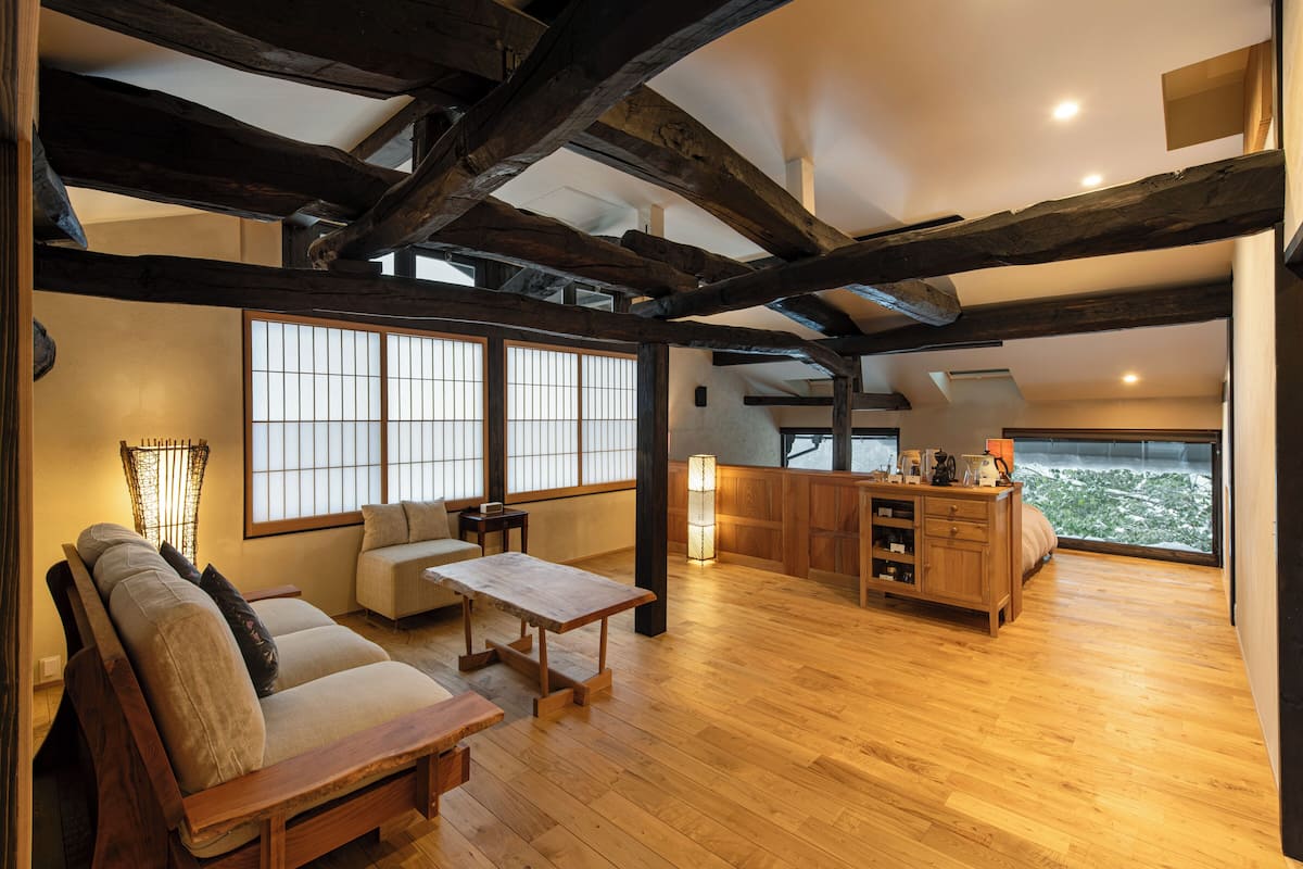 Een ruime woonkamer met houten balken, een bank, een salontafel en uitzicht door grote ramen.