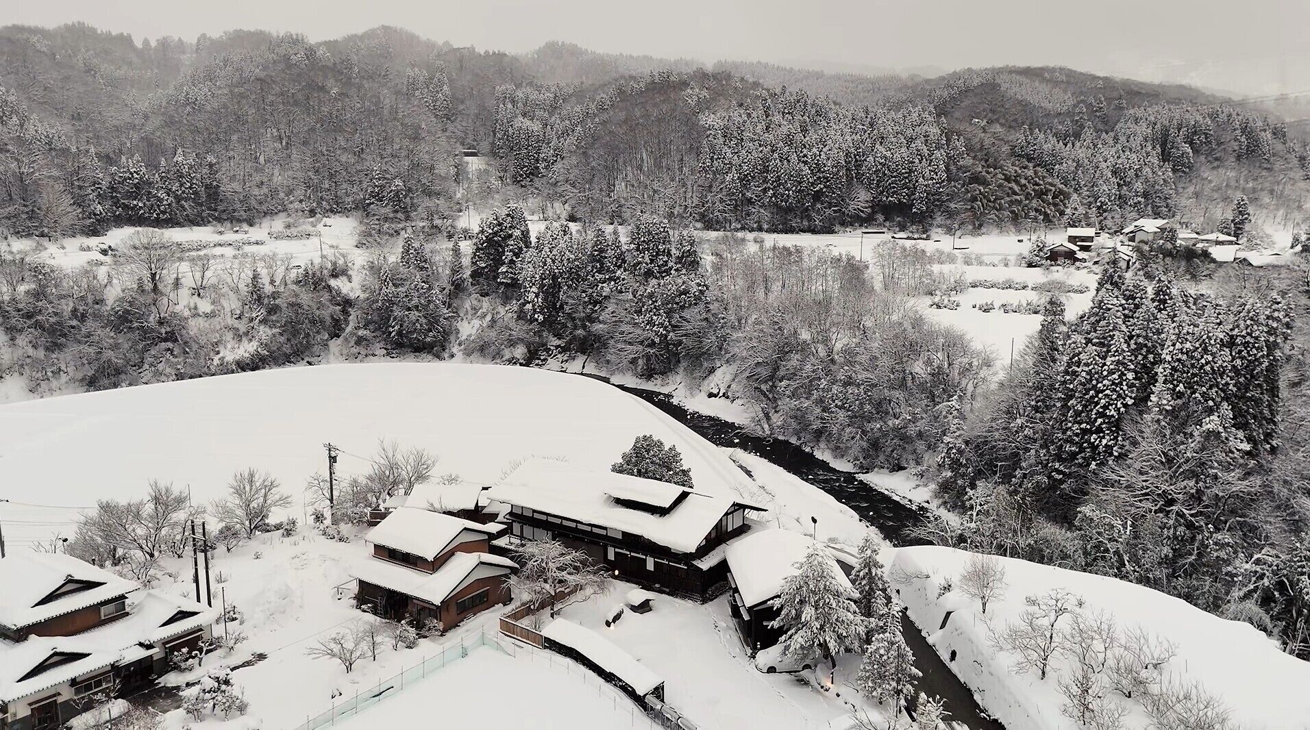 Uma casa tradicional japonesa cercada por árvores e colinas cobertas de neve.