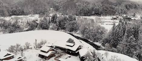 Uma casa tradicional japonesa cercada por árvores e colinas cobertas de neve.