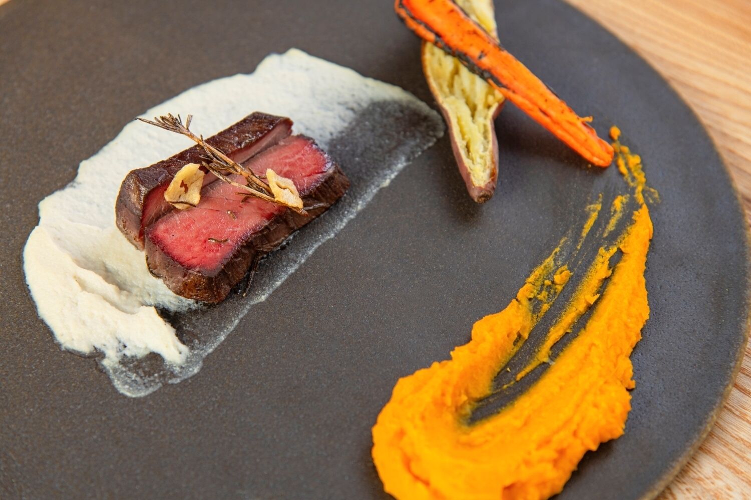 A plate with a piece of meat, a sweet potato, and a creamy substance.