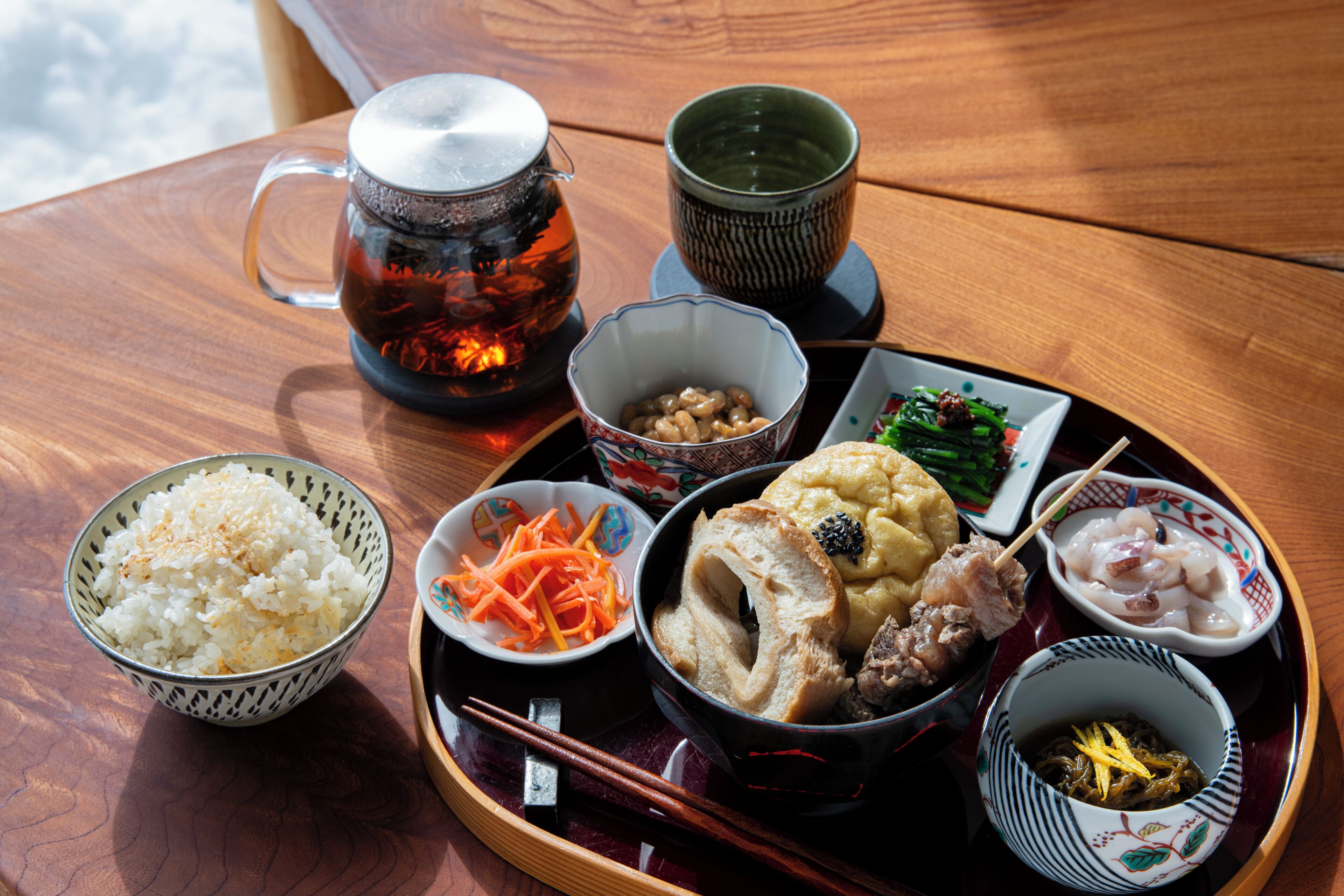 A tray with various dishes including rice, vegetables, and meat, accompanied by a teapot and cups.