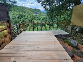 Terraza de madera con valla de bambú con vista a un bosque exuberante.