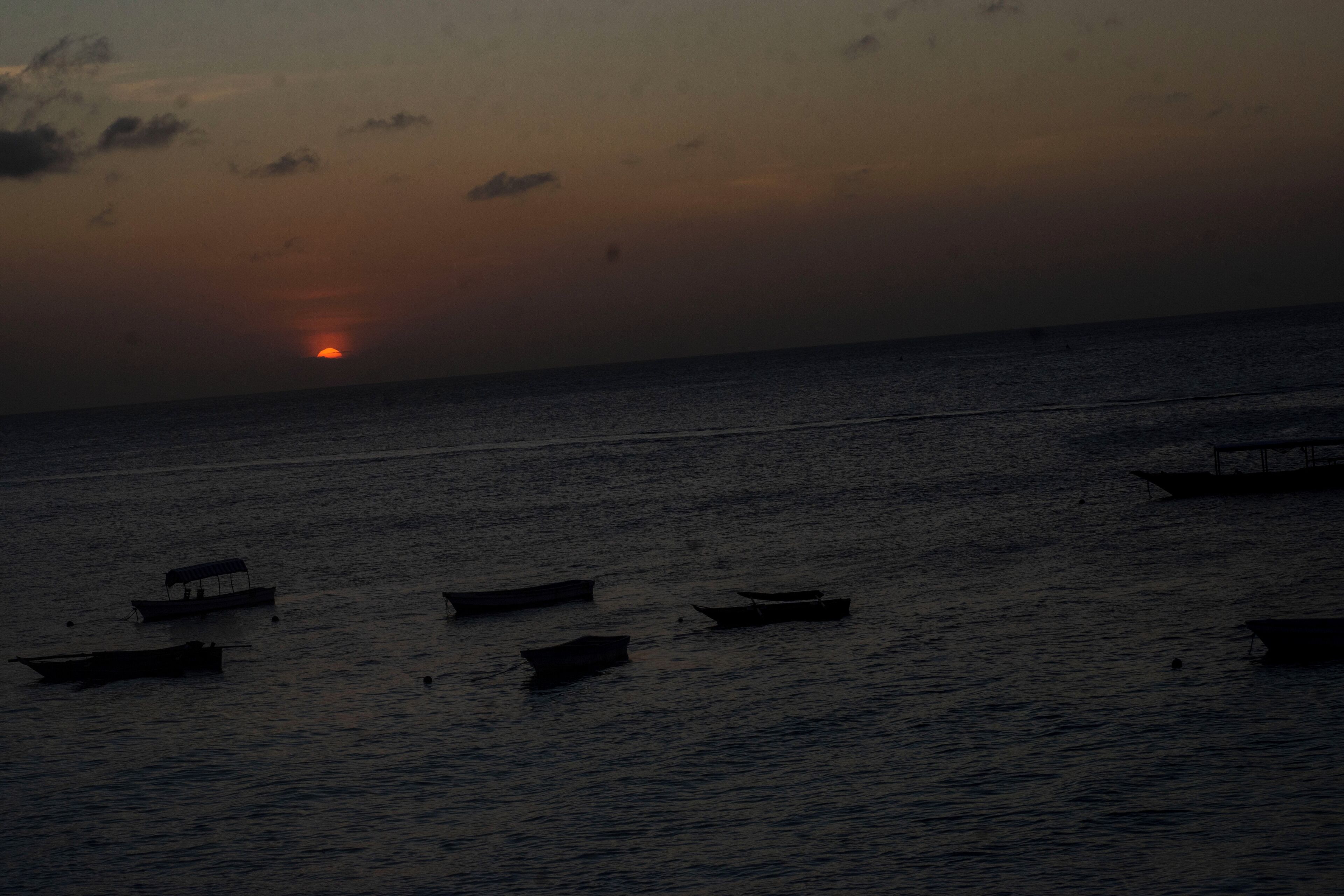 A sunset over a calm sea with several small boats.