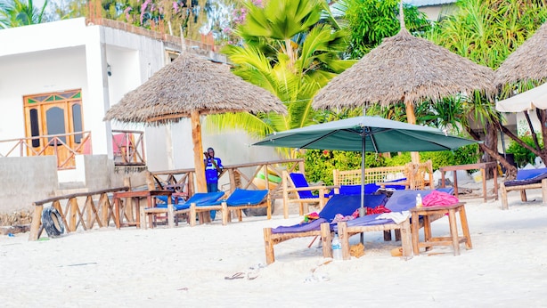 Een strandlounge met rieten parasols, loungestoelen en een kleine tafel.