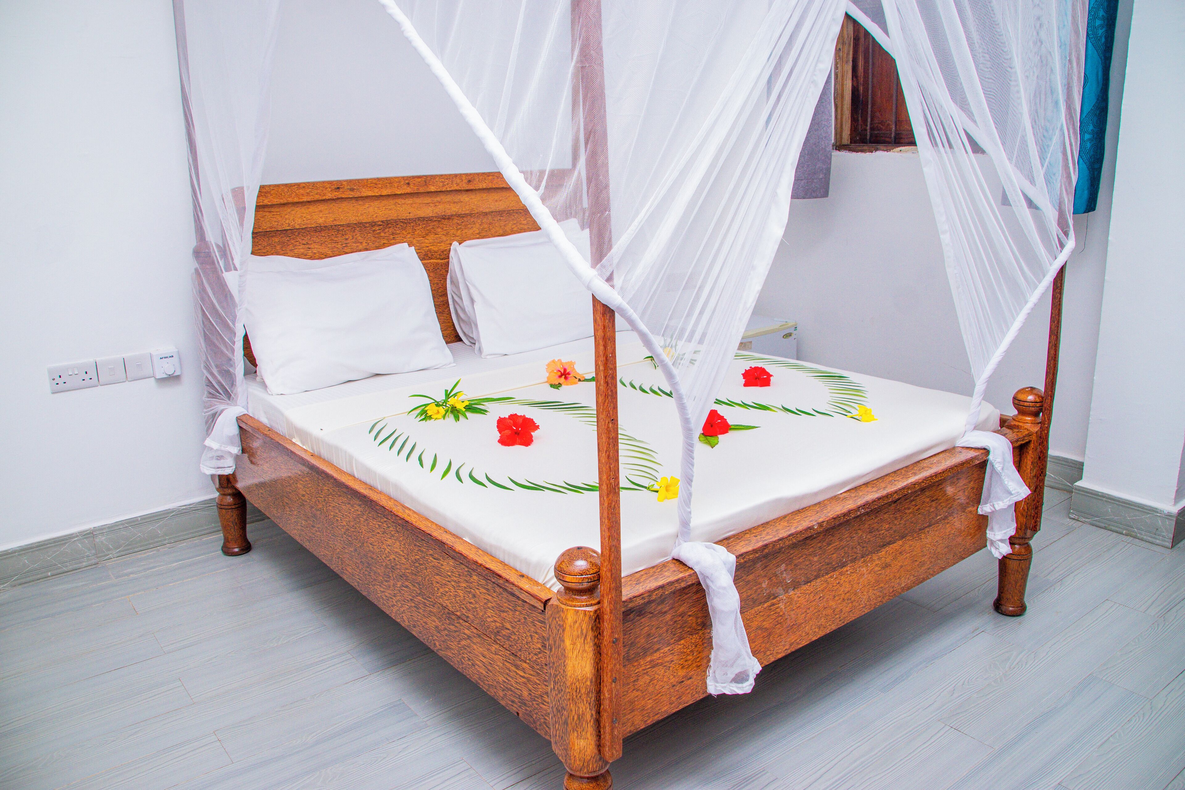 A wooden four-poster bed with a white canopy, a floral bedspread, and a white pillow.