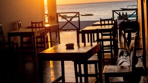 Een restaurant met houten tafels en stoelen, een uitzicht op de oceaan en een zonsondergang op de achtergrond.
