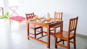 Een houten eettafel met stoelen, een rode mat en diverse ontbijtartikelen.