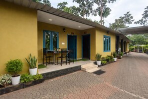 Un edificio amarillo con puertas de marco azul, un camino pavimentado y macetas con plantas.