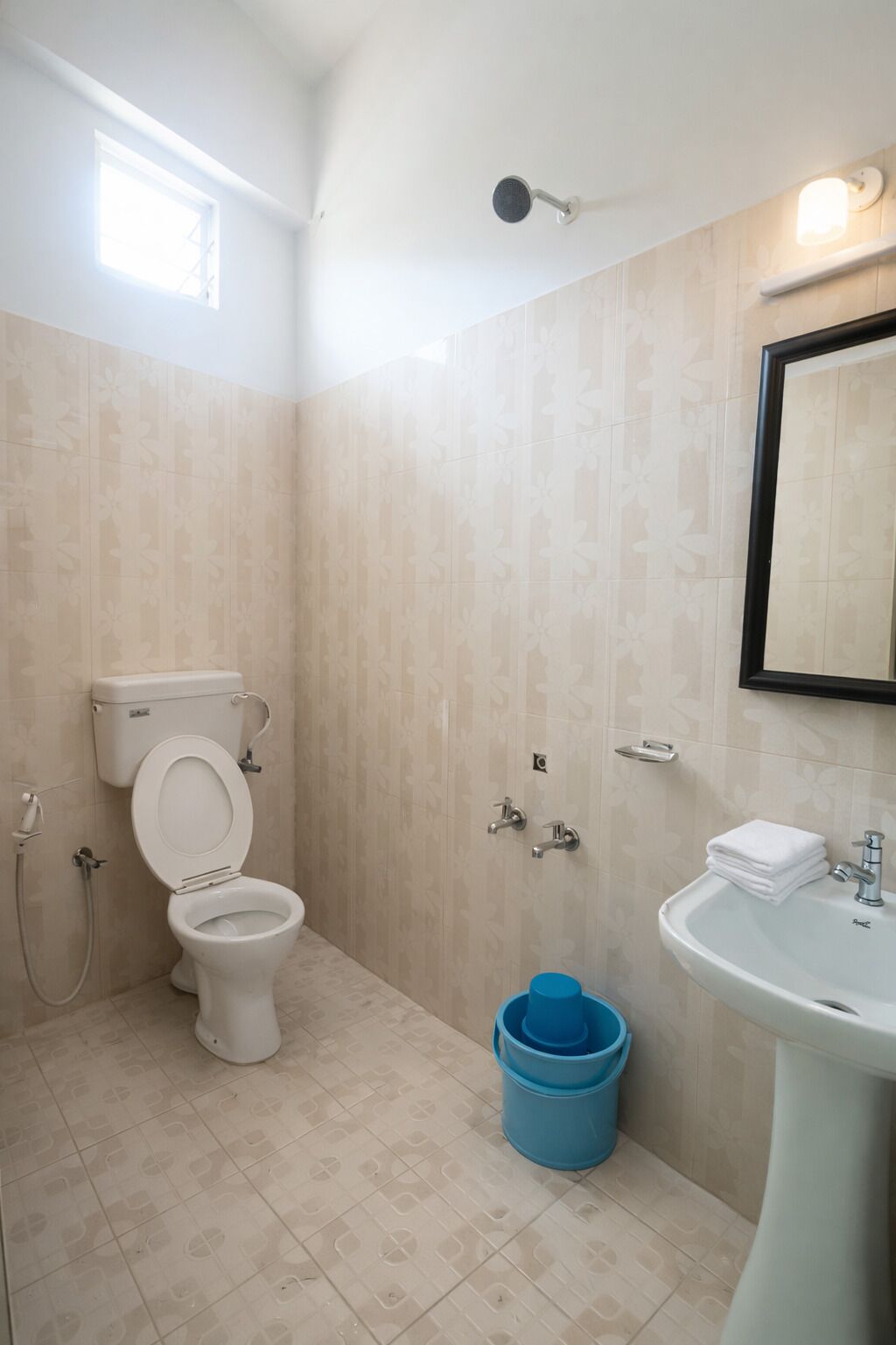 Un baño con inodoro, bidé, lavamanos y un cubo azul.