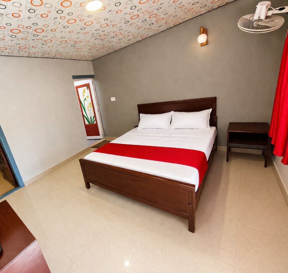 Ein Hotelzimmer mit einem hölzernen Bett, einem Nachttisch, einem Wandventilator und einer dekorativen Decke.