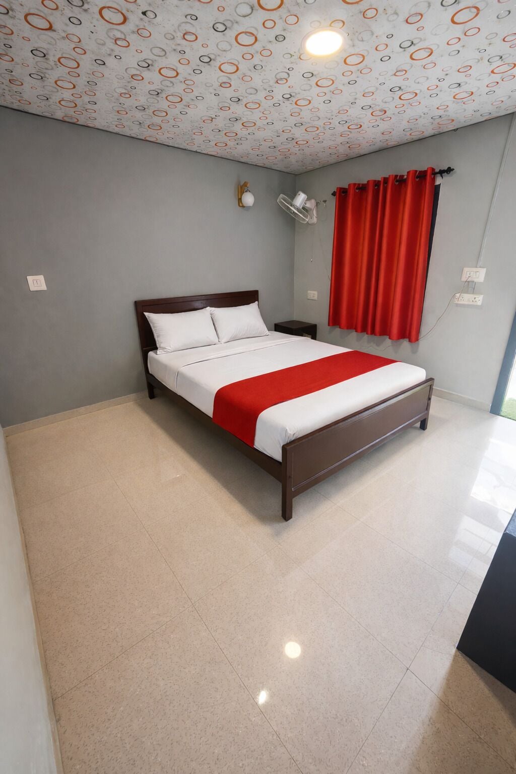 A neatly made bed with a red blanket, a wooden headboard, and a patterned ceiling.