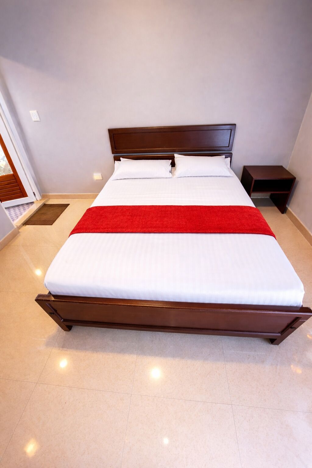 A neatly made bed with a wooden headboard, a red throw blanket, and a small bedside table.