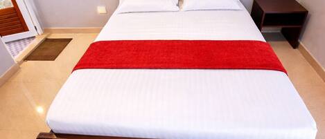 A neatly made bed with a wooden headboard, a red throw blanket, and a small bedside table.