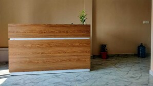 A reception desk with a wooden finish and a white accent strip, a potted plant on top, and a marble floor. - RIVER SIDE HOTEL PRAYGRAJ (Phulpur)