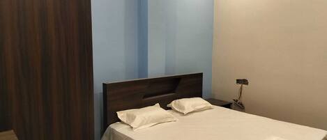 A bedroom with a bed, a nightstand, and a wooden wardrobe.