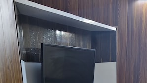 A corner of a room with a wooden wall, a black TV on a shelf, a white electrical outlet, and a black trash bin. - RIVER SIDE HOTEL PRAYGRAJ (Phulpur)