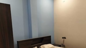 A neatly made bed with white linens in a room with blue walls and a wooden floor. - RIVER SIDE HOTEL PRAYGRAJ (Phulpur)