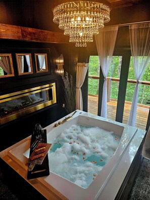 Un bagno lussuoso con una grande vasca da bagno, un lampadario e vista sul verde circostante.
