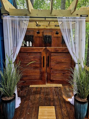 L'ingresso di una baita di legno con un portico coperto, due vasi con piante e una panchina.