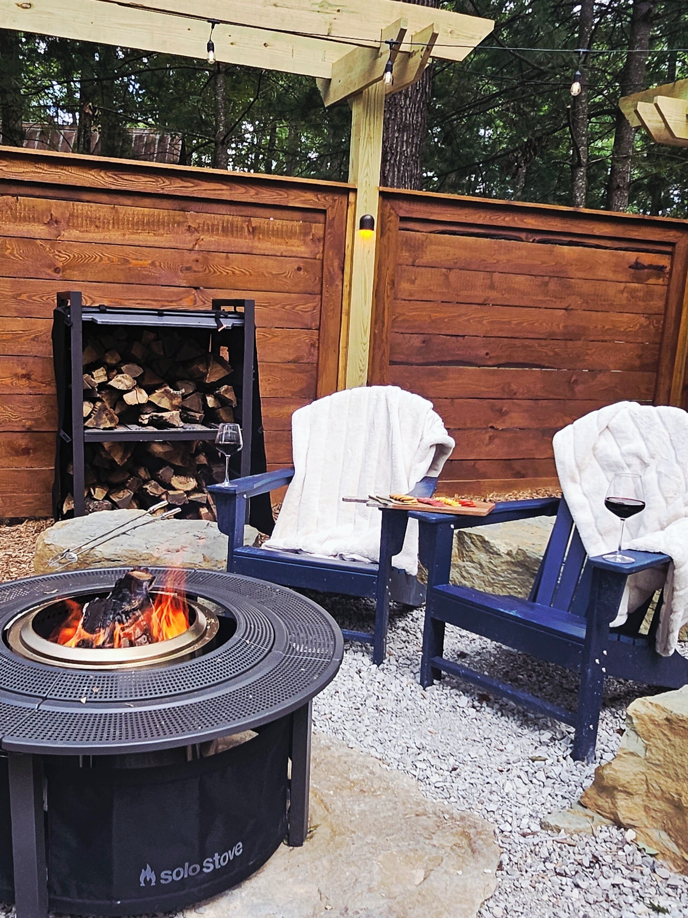 Un espace patio avec un foyer, deux chaises bleues et une clôture en bois.