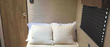 A bedroom with a bed, a TV mounted on the wall, and a window with blinds.