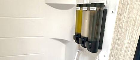 A bathroom with a white tiled wall, a white sink with a soap dispenser, and a shower area.