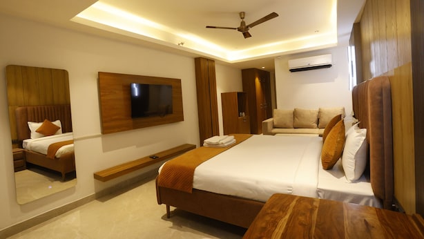 A modern hotel room with a large bed, a flat-screen TV mounted on the wall, a ceiling fan, and a wooden headboard. - The Hoften Lotus Court Noida (Noida)