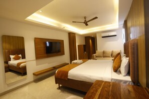 A modern hotel room with a large bed, a flat-screen TV mounted on the wall, a ceiling fan, and a wooden headboard. - The Hoften Lotus Court Noida (Noida)