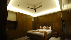 A modern bedroom with a large bed, wooden paneling, a ceiling fan, and a small bedside table. - The Hoften Lotus Court Noida (Noida)