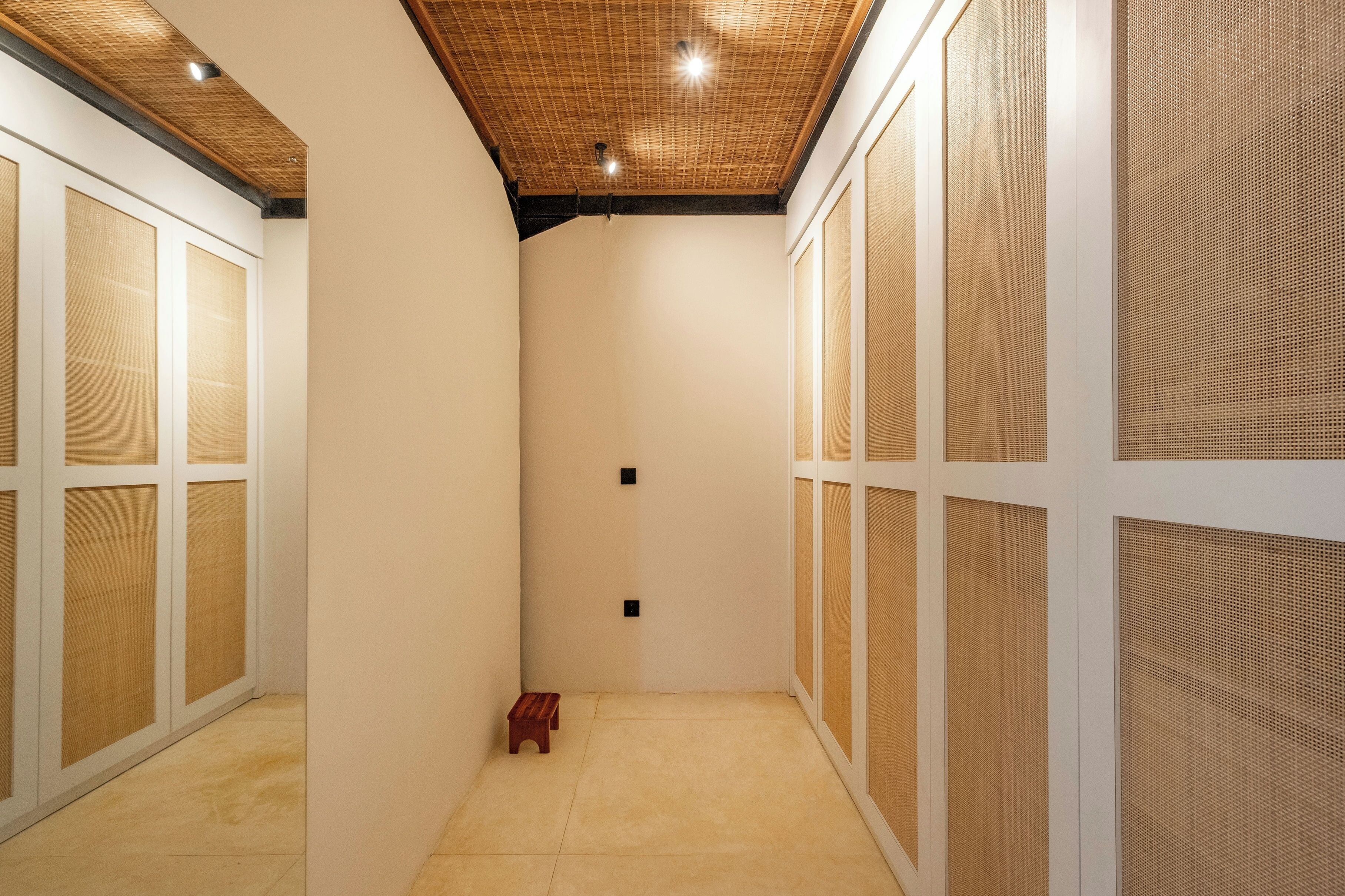 Un couloir étroit avec un plafond en bois, des murs blancs et un petit tabouret en bois.