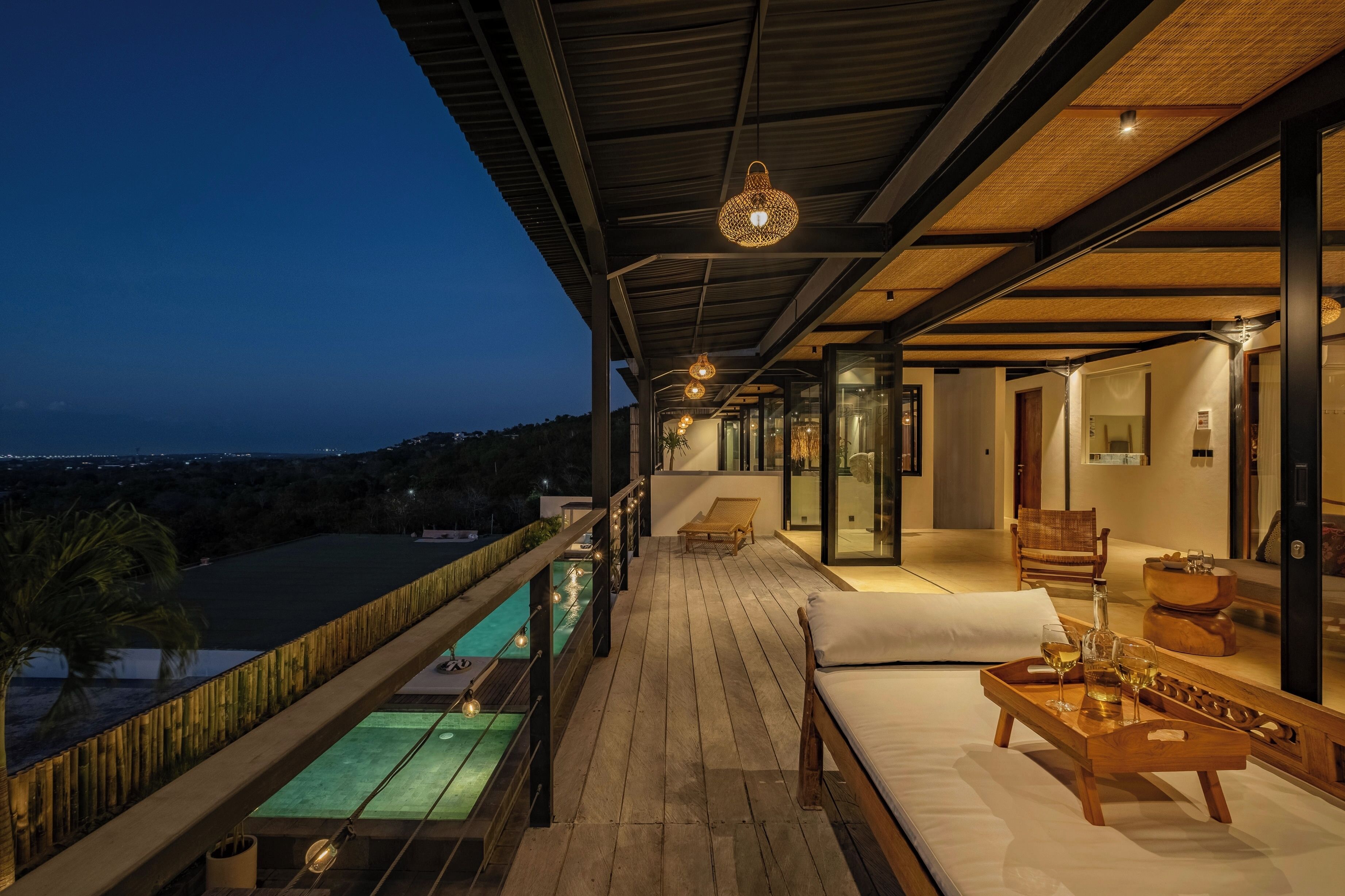 A wooden deck with a pool, lounge chairs, and a table with drinks.