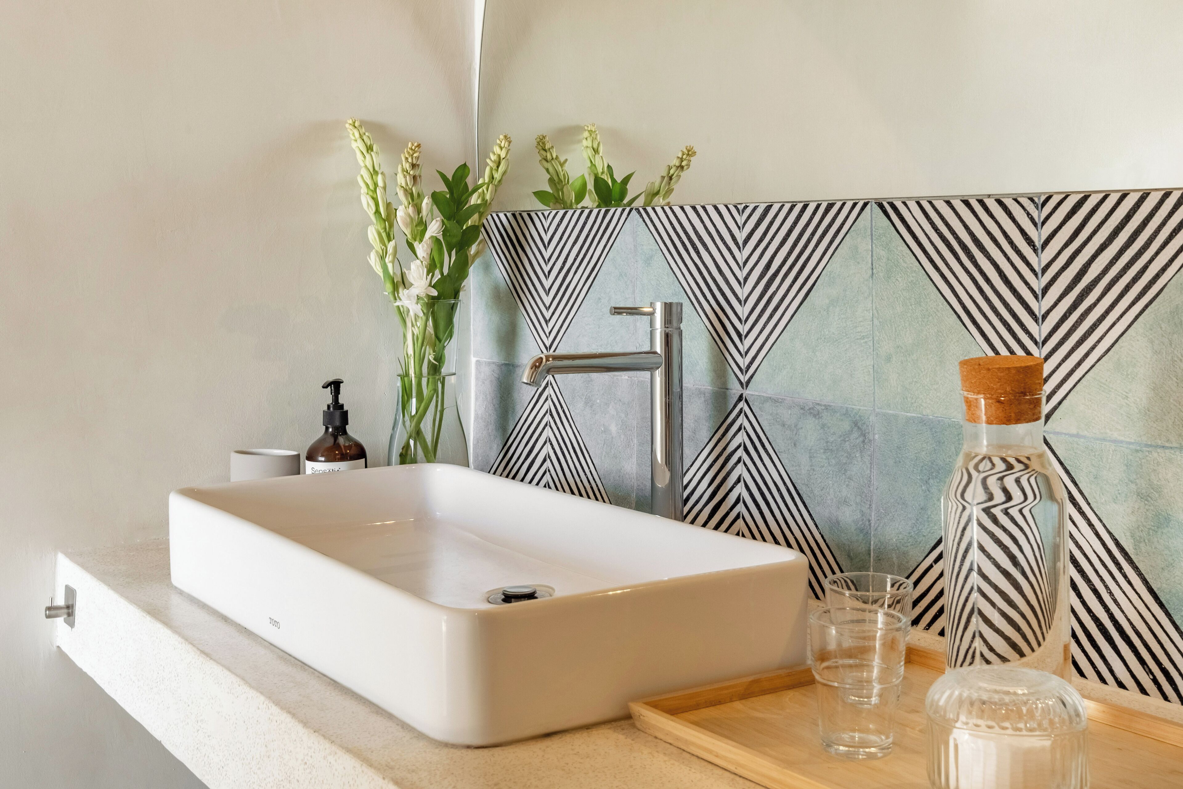 Un bagno con un lavandino bianco, uno specchio, un erogatore di sapone e una pianta decorativa.