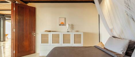 A bedroom with a bed, a white cabinet with woven panels, a door, and a wall-mounted picture.