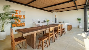 Une cuisine spacieuse avec une longue table et des chaises en bois, une grande plante en pot et un îlot central.