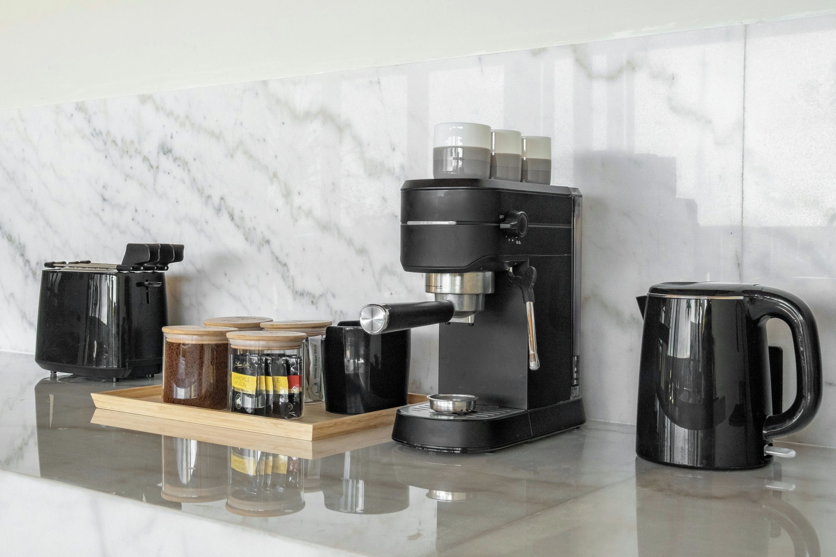 A kitchen with a coffee machine, a kettle, and jars on a tray.