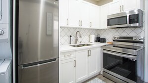 A modern kitchen with white cabinets, stainless steel appliances including a refrigerator, microwave, and oven, and a tiled backsplash.