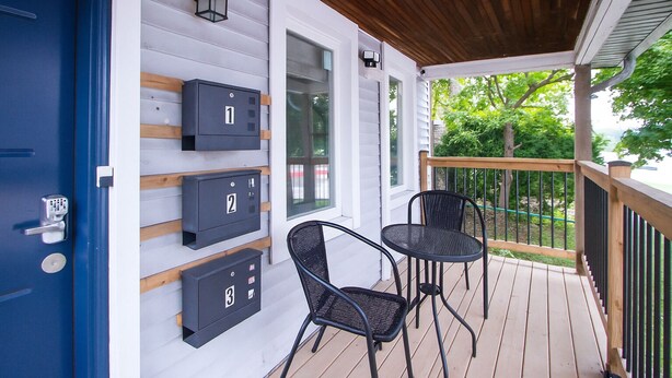 A covered porch with three mailboxes, two chairs, and a wooden railing.