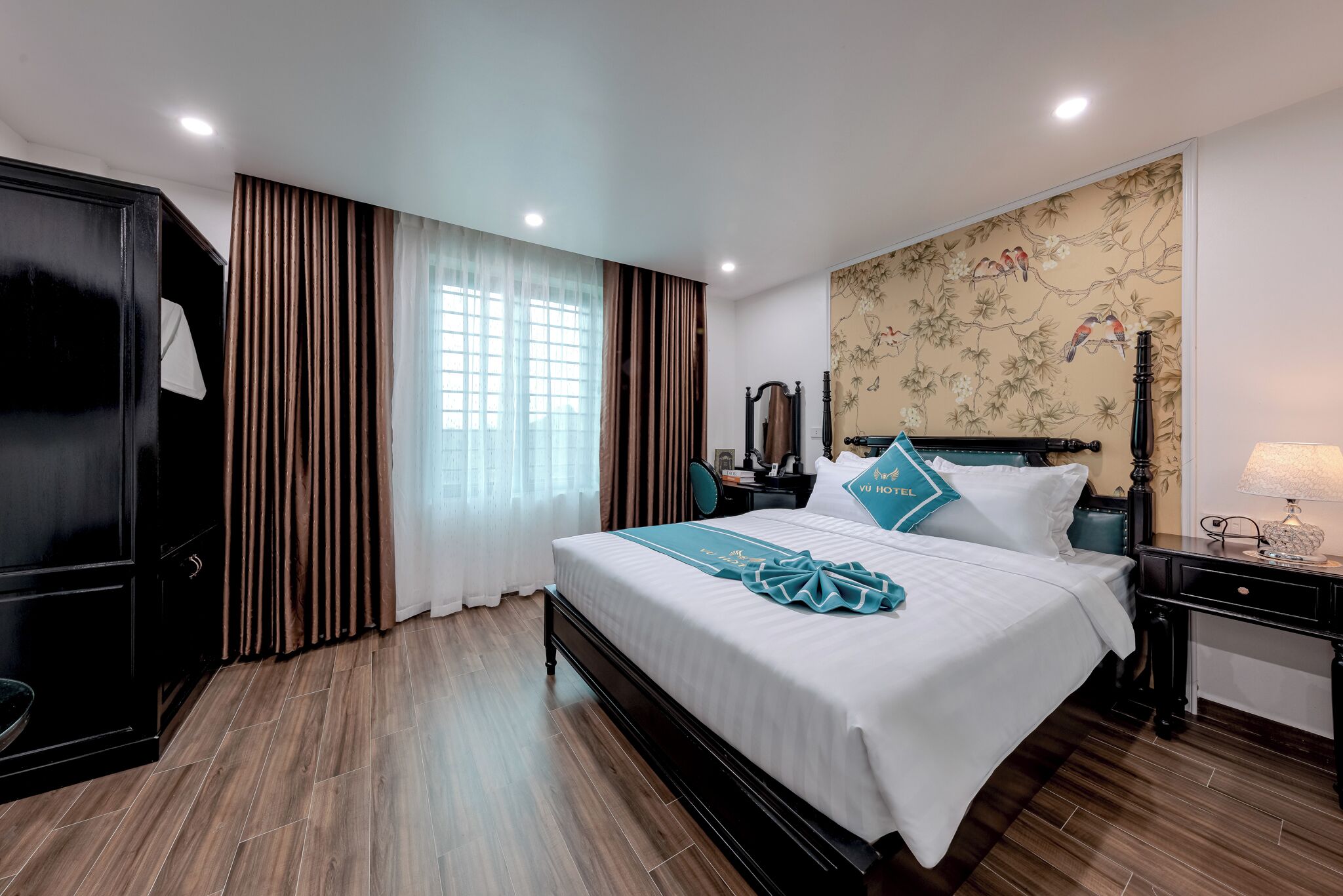 Habitación de hotel con una cama grande, un armario, un escritorio con lámpara y una pared con un mural floral.