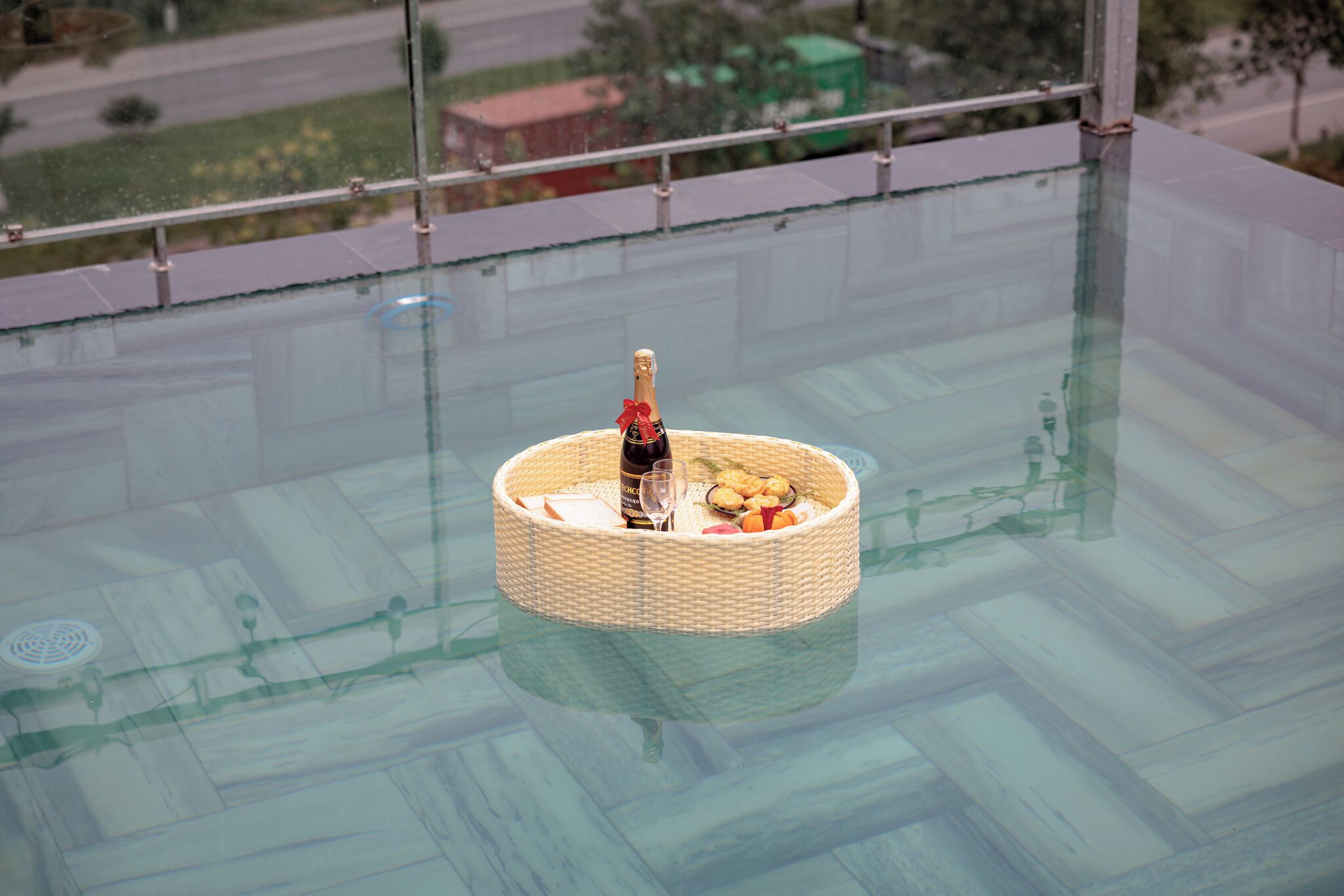 A glass table with a woven basket containing a bottle and snacks.