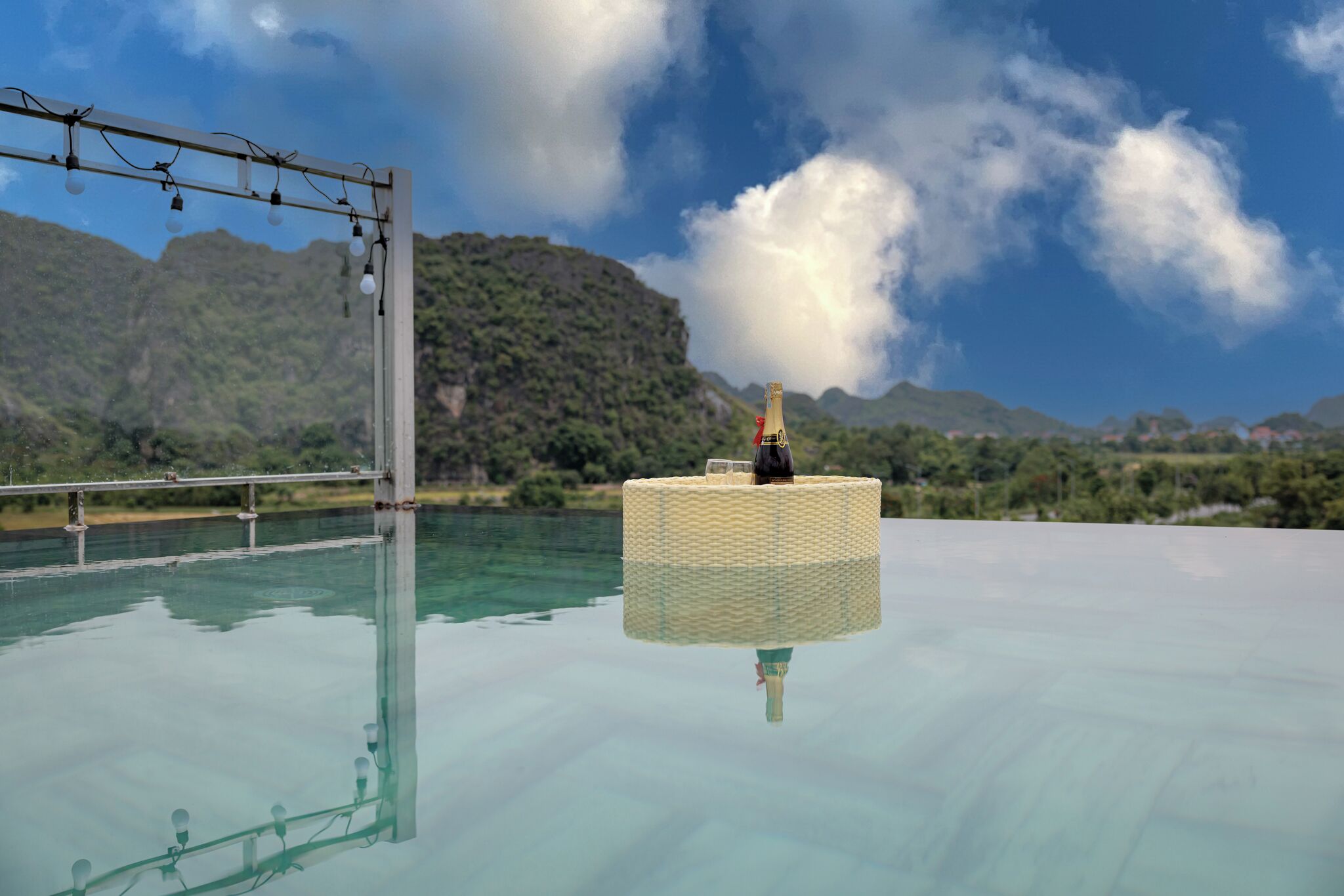 A glass-bottomed pool with a wicker chair and a bottle of champagne, surrounded by mountains and a clear sky.